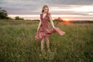 A flowy pink dress catches the breeze in a grassy field at sunset as golden light streams across the meadow.