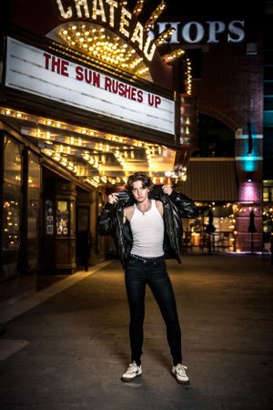 Nighttime portrait in front of illuminated Chateau theater marquee displaying 'The Sun Rushes Up' in lights.