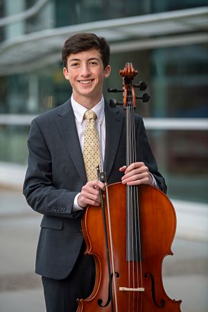 Formal portrait of musician holding cello in grey suit with yellow tie.