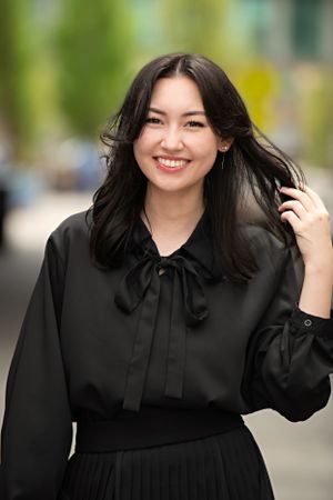A smiling person wearing a black bow-tied blouse with flowing dark hair against a blurred background.