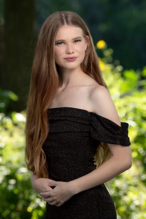 Elegant portrait in black off-shoulder dress against garden background.