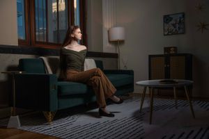 Moody interior scene with person seated on teal couch in dramatic lighting.