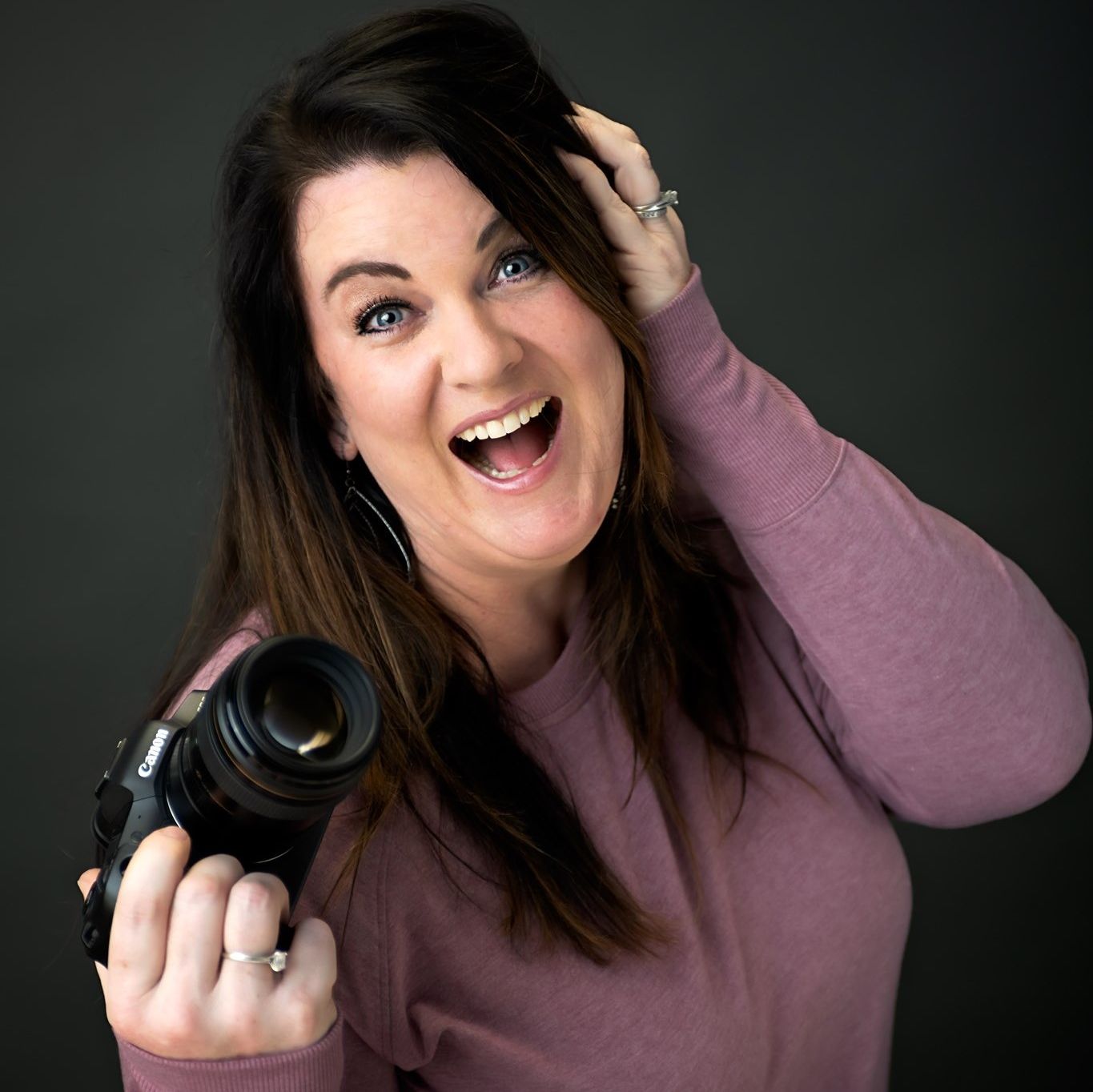 Portrait of woman with vibrant red hair wearing purple top against neutral background.