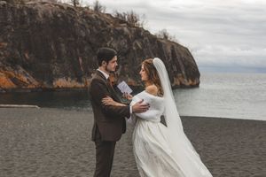 A couple embraces during their winter wedding ceremony against a dramatic coastal backdrop of cliffs and water.