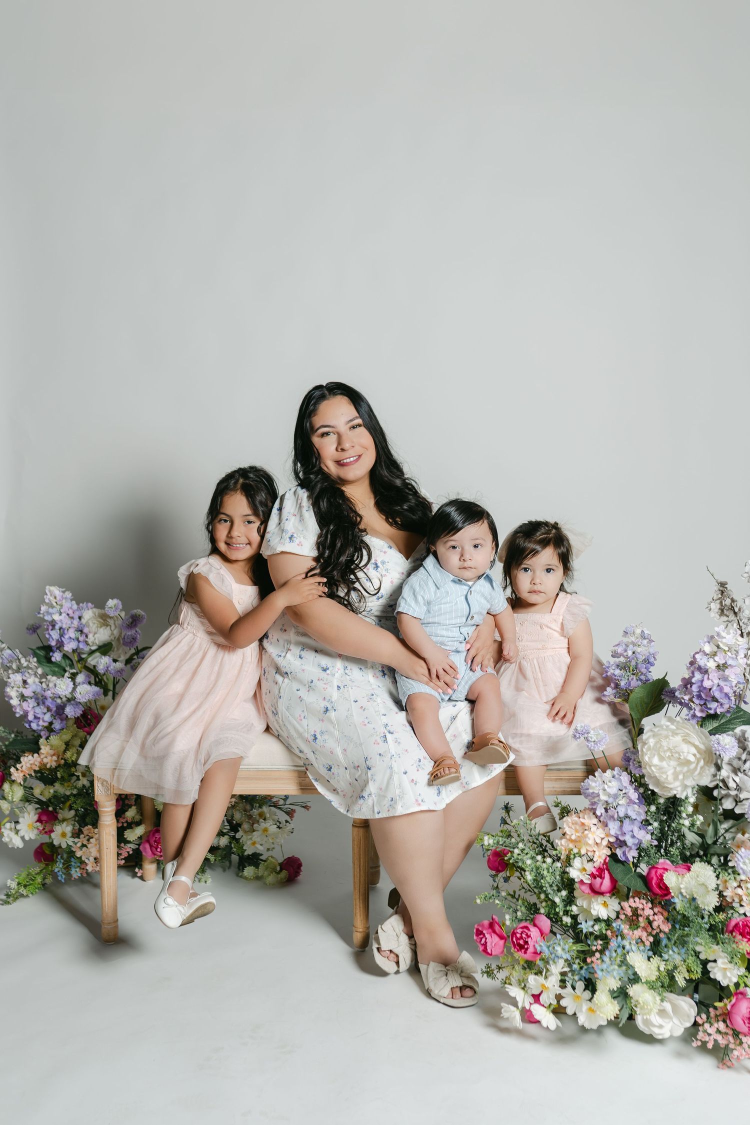 A family portrait shows mother and children sitting on a bench surrounded by pink, purple and white floral arrangements.