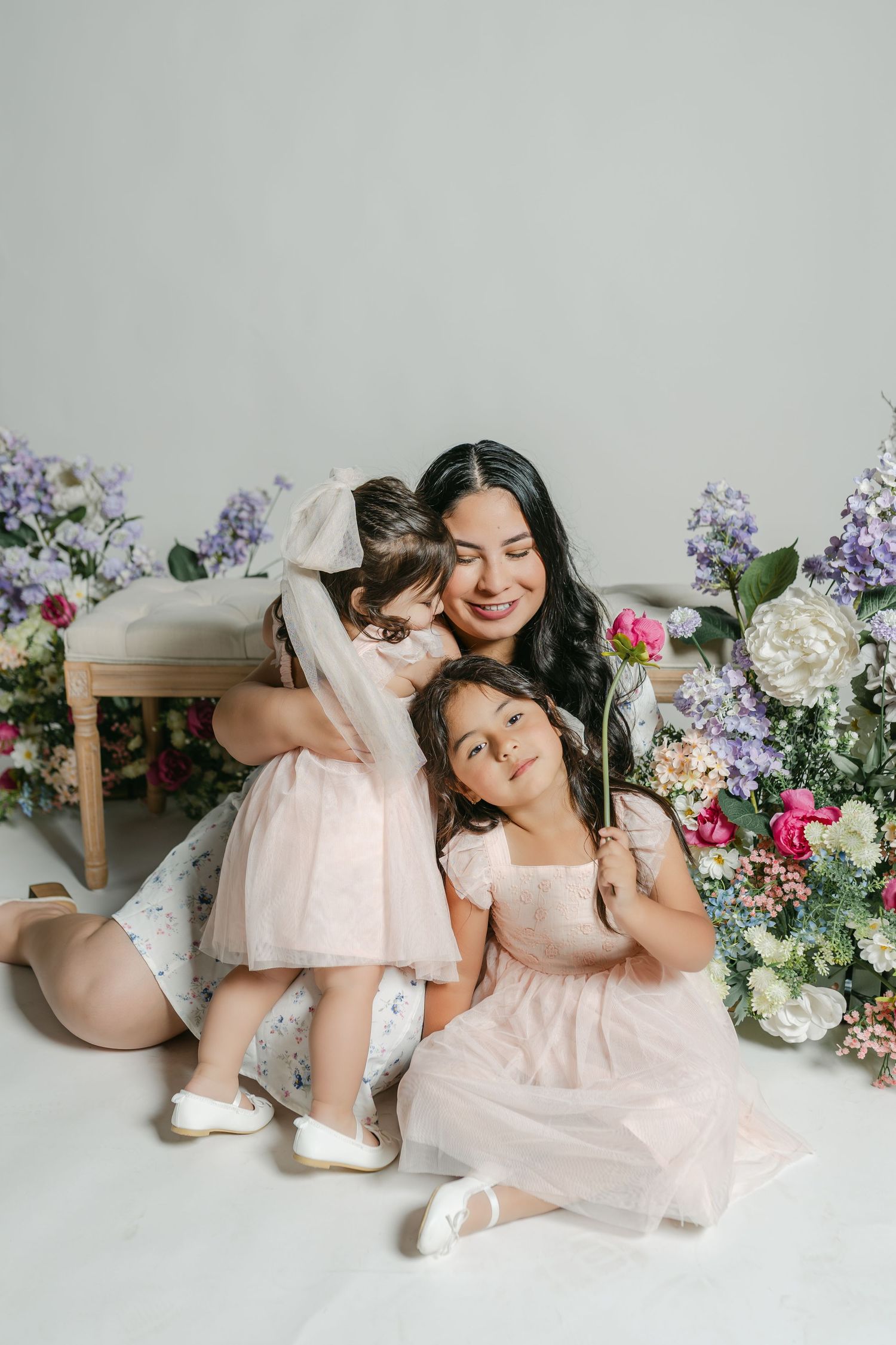 A dreamy spring portrait features pastel dresses and floral arrangements with purple and pink blooms.
