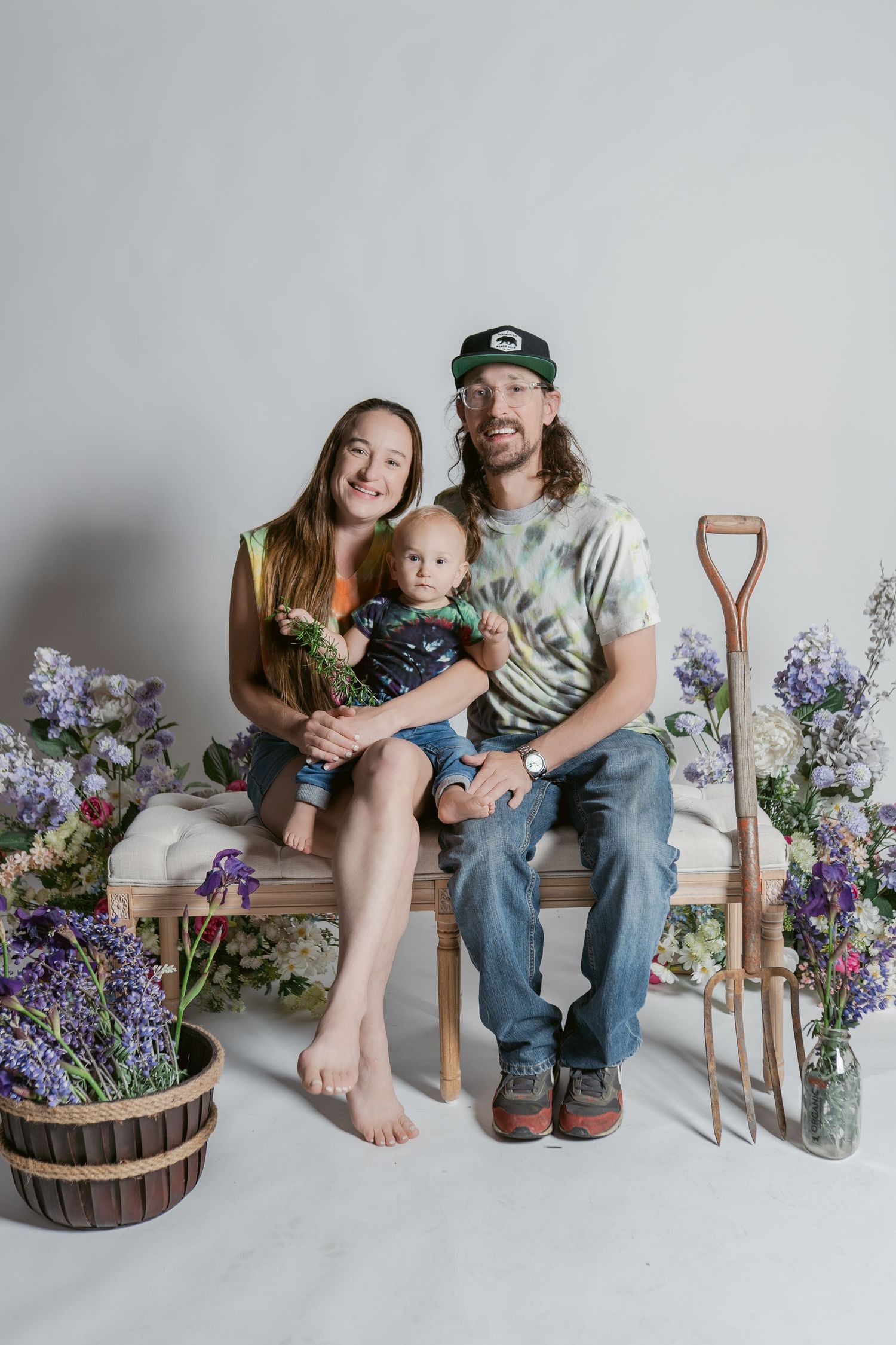 A family photo in a rustic setting with wooden baskets of purple flowers and a garden shovel as props against white backdrop.