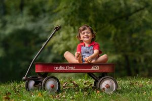 small boy plays with toes in vintage red wagon