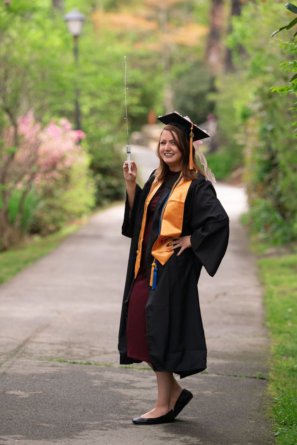 Nursing Graduate poses with syringe along outdoor walkway