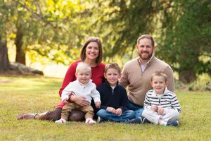 family of 5 smiles at camera in posed photo sitting in the grass.