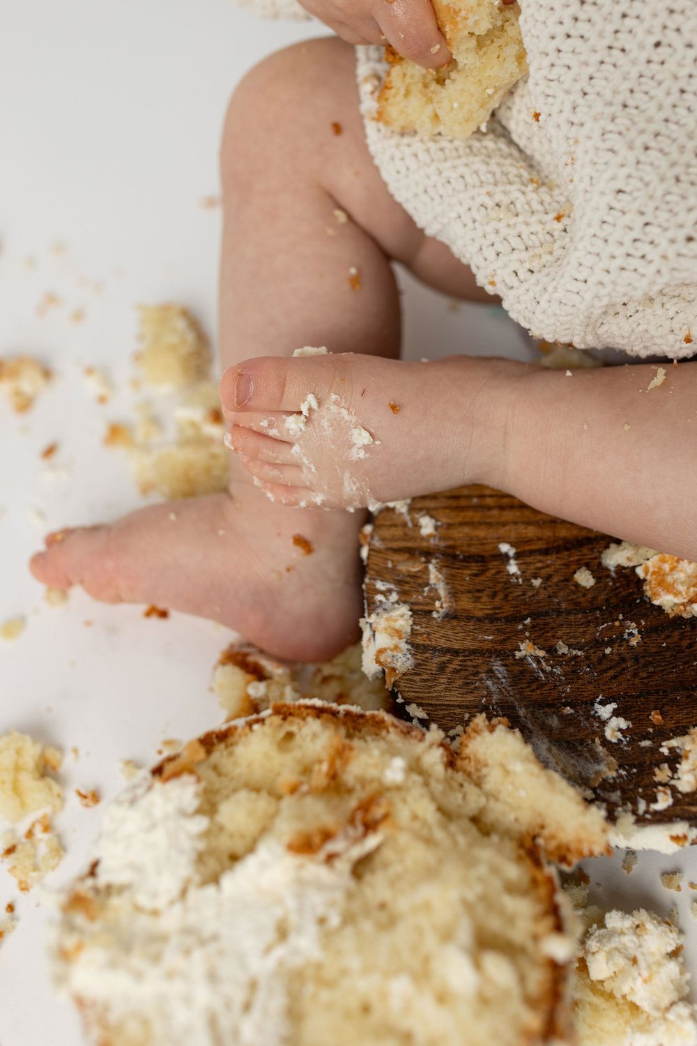 Baby feet and hands covered in cake crumbs during a first birthday cake smash photoshoot.