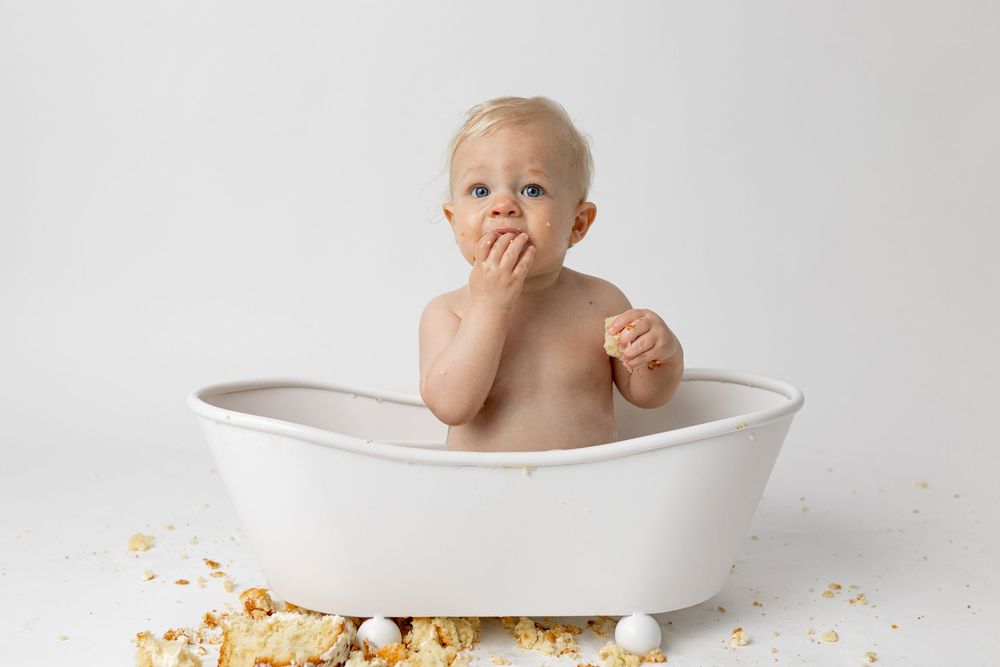 Cute baby sitting in a small white bathtub surrounded by cake crumbs during a cake smash photo shoot.