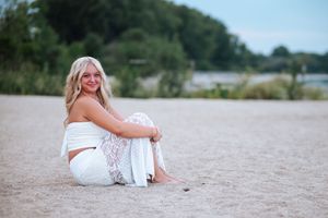 A person in white attire sits on a sandy beach during a summer evening photoshoot.