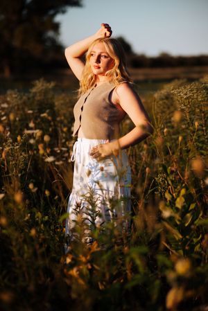 A person in a white dress stands among wildflowers at golden hour in a dreamy summer meadow.
