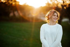 Golden hour portrait in white sweater with natural backlit glow.
