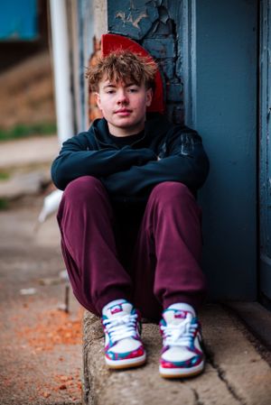 Person in casual attire sits on concrete ledge against blue and red painted wall.