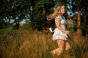 A person in a denim vest and white dress twirls joyfully through a sunlit meadow of tall grass at golden hour at Maumee Bay State Park.