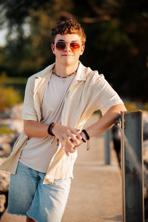 Person in sunglasses and light colored shirt poses casually outdoors during golden hour lighting.