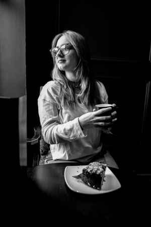 Black and white portrait of person enjoying coffee and dessert in moody lighting.