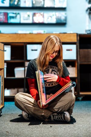 Person in casual attire sitting cross-legged on floor browsing through photo albums.