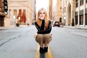 Urban portrait of person crouching on yellow street line wearing black sweater.