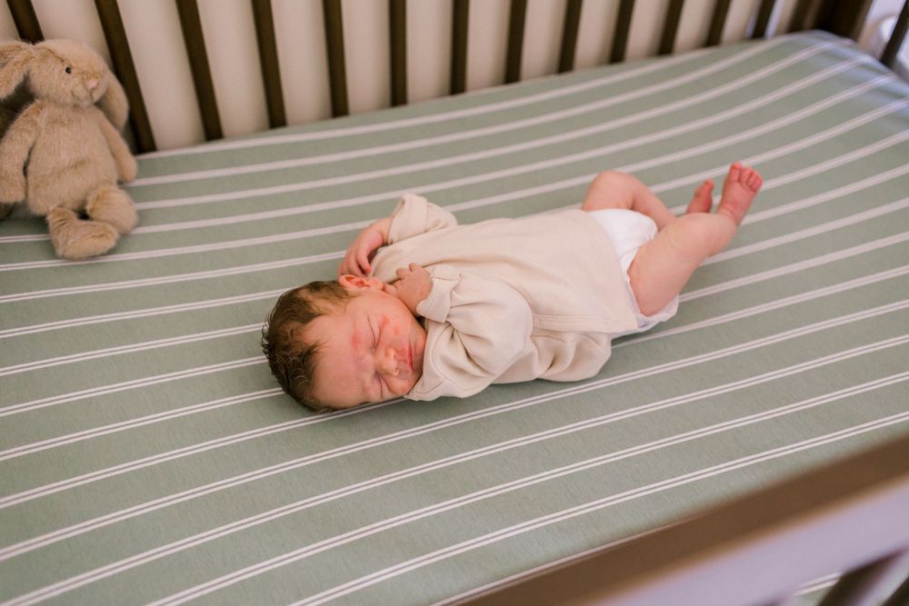 Newborn baby sleeping peacefully in a crib on green striped sheets with a stuffed bunny nearby, in Indiana.