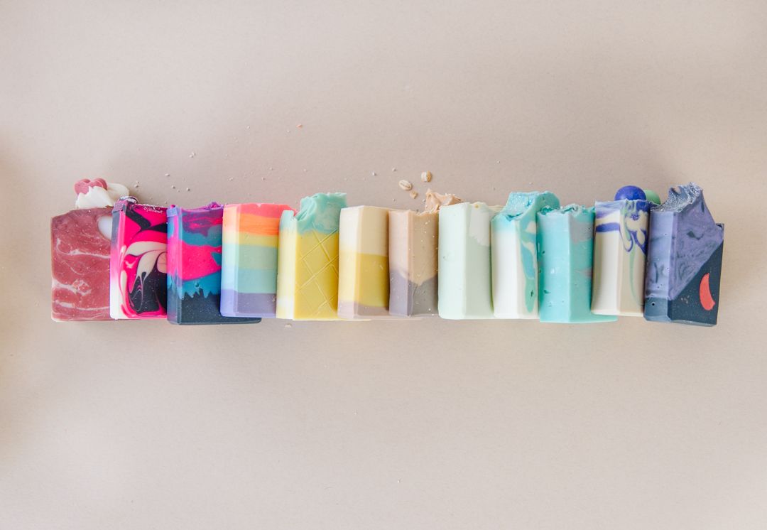 Row of colorful soap bars arranged in rainbow gradient pattern on white wall.
