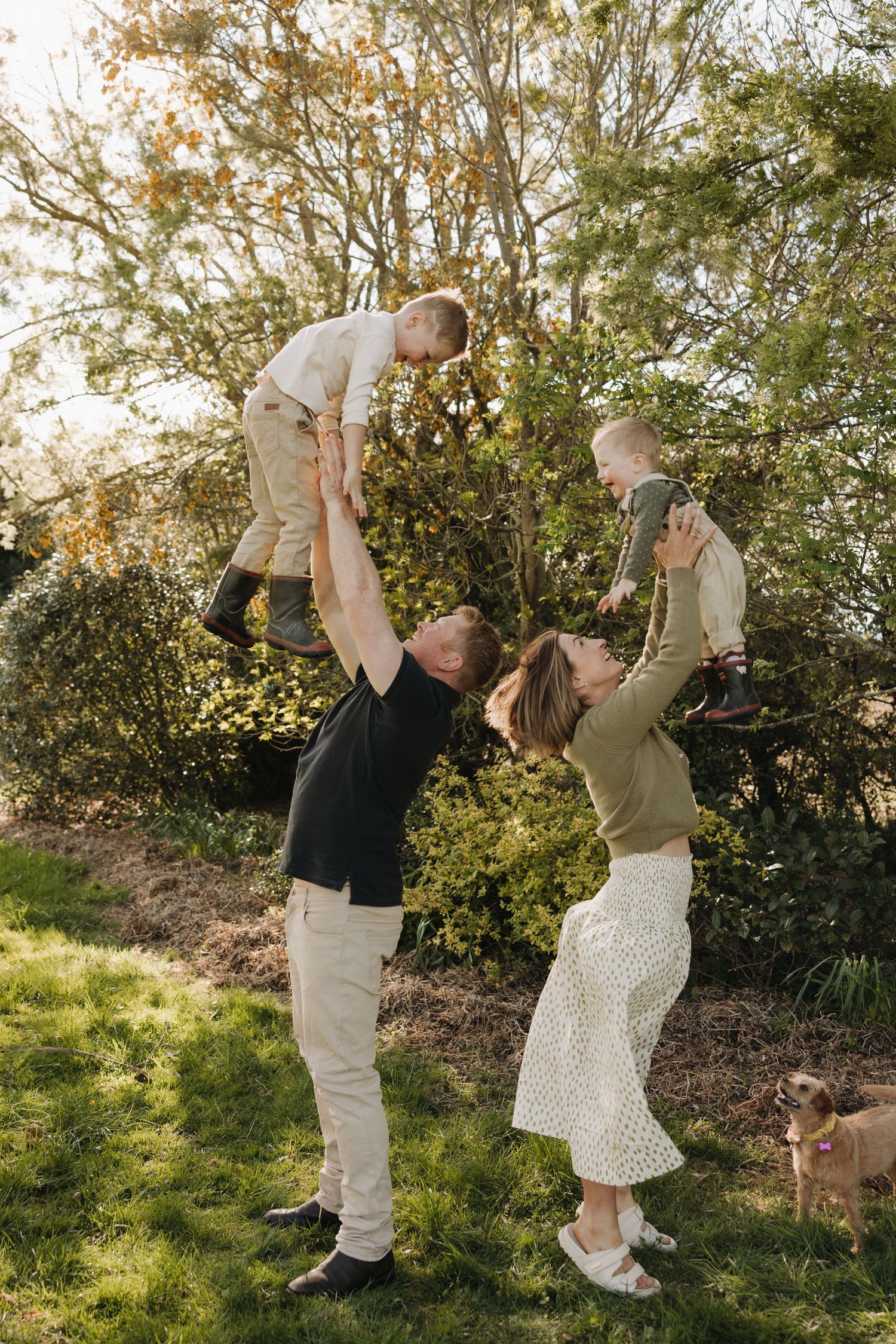 A joyful outdoor family photoshoot showing playful lifting moments in a garden setting.