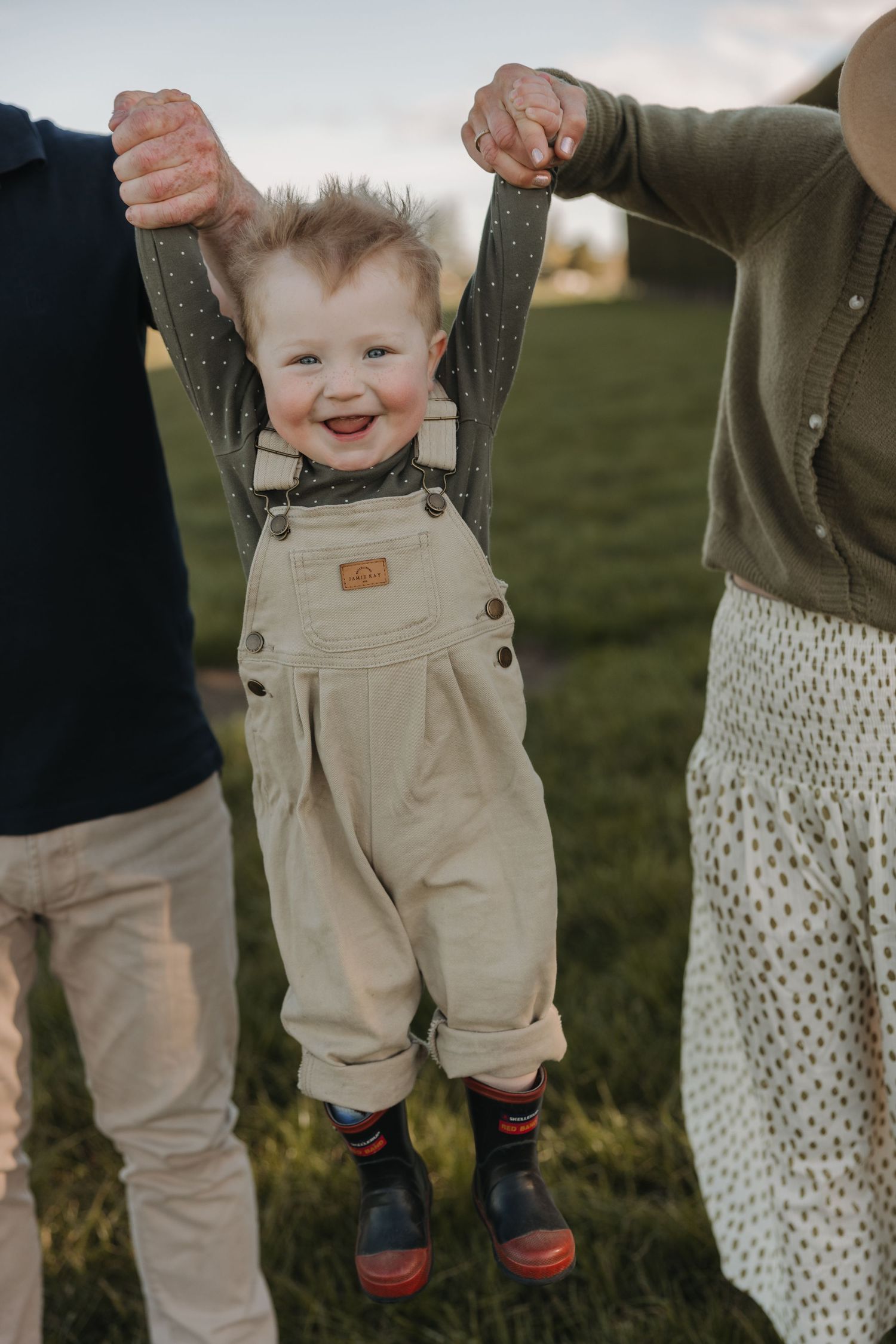 A sequence showing a smiling toddler in beige overalls being lifted up against a natural outdoor backdrop.