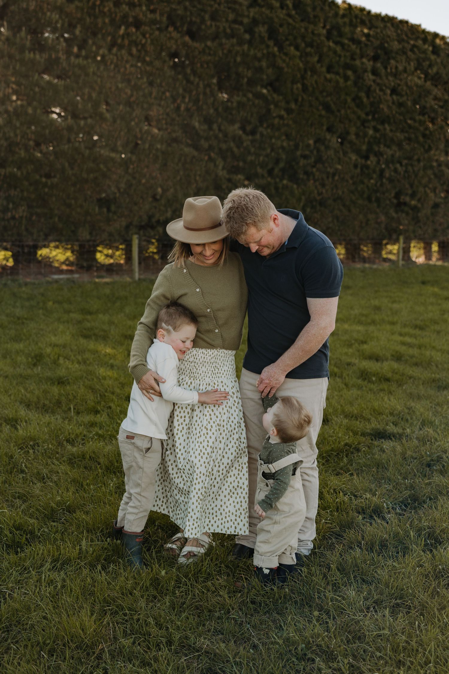 A family shares an intimate moment together while standing in a grassy field at sunset.