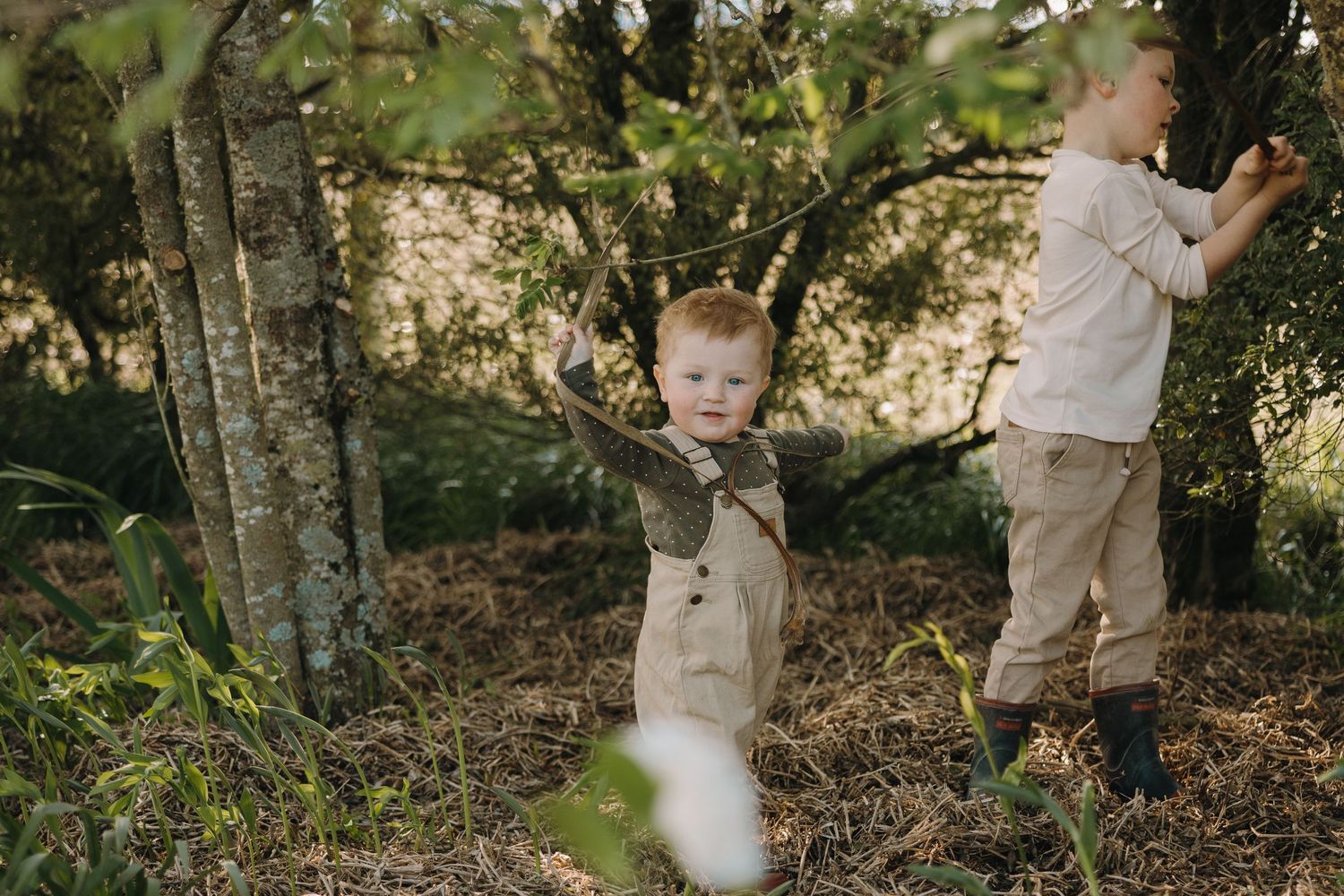 Candid outdoor family photo session in a wooded area with natural lighting and rustic earth tones.