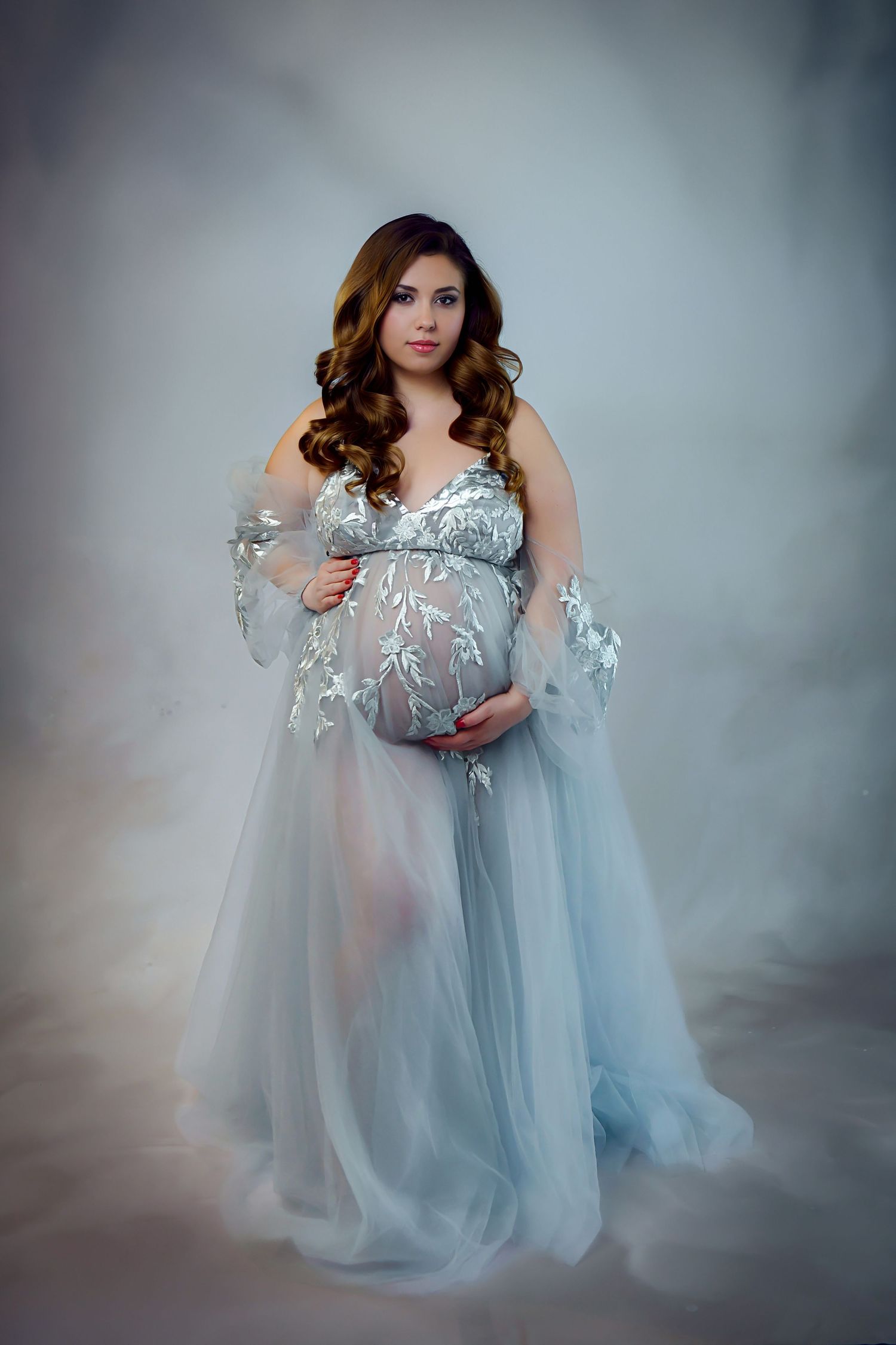 A dreamy maternity photoshoot featuring an ethereal light blue tulle gown against a misty gray backdrop.