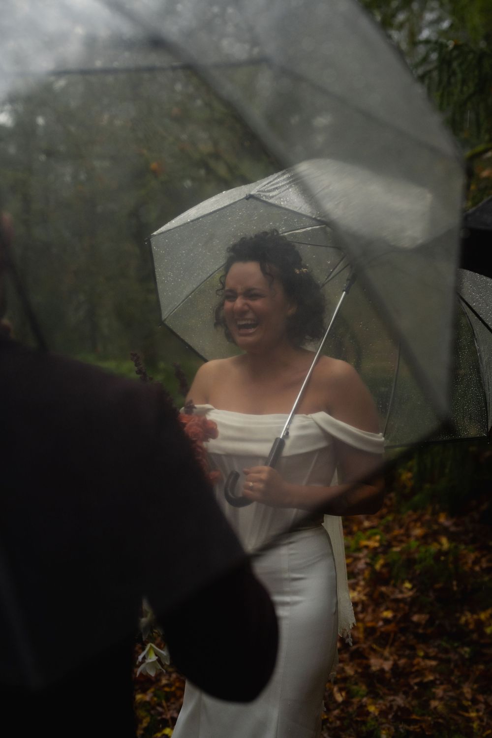 A joyful moment captured under clear umbrellas in a moody forest setting.