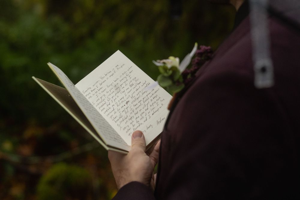 A hand holds open a book against a dark blurred background showing handwritten text on its pages.