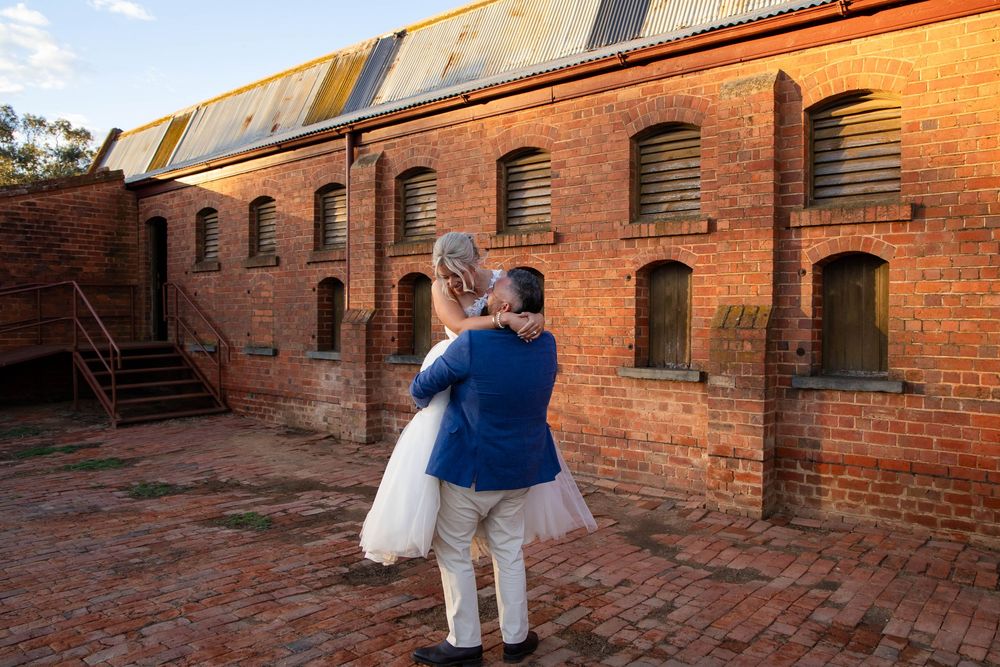 People walk through a historic brick courtyard at sunset with golden light illuminating the arched architecture.