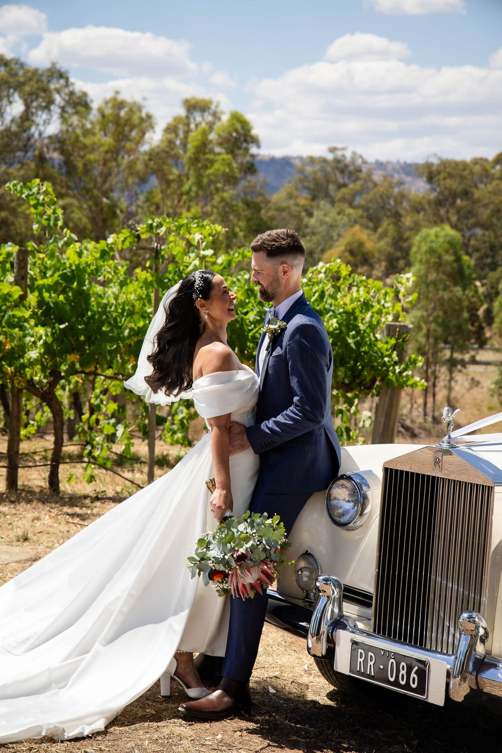 A classic Rolls Royce parked in a vineyard setting during a wedding photo session with flowing white veil in motion.