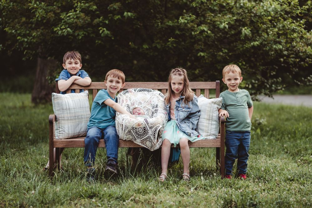 Four young children sitting and laughing together on a vintage wooden bench outdoors.