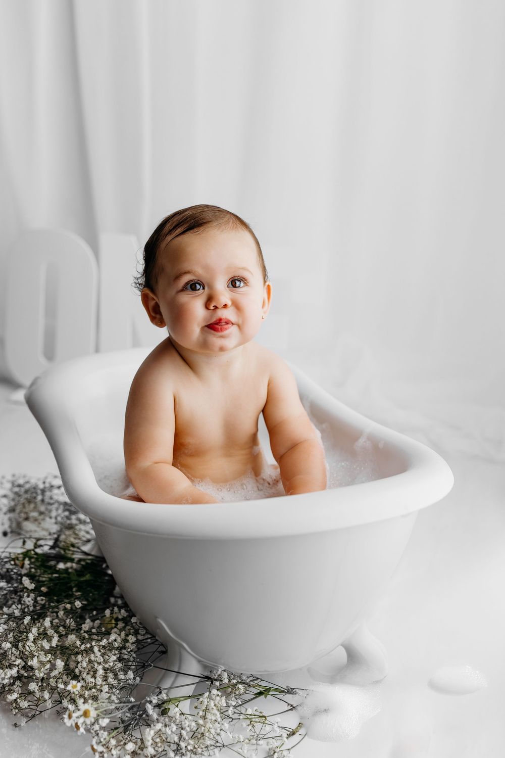 A series of four photos showing a baby taking a bath in a white ceramic tub surrounded by delicate baby's breath flowers.