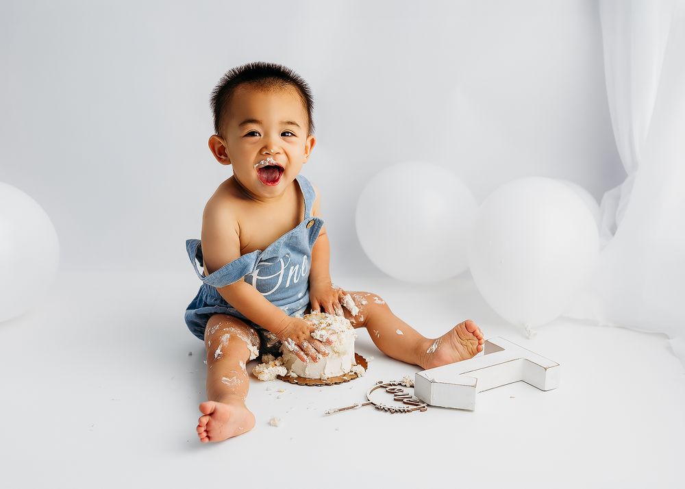 A baby in a white onesie sits on a white background while making various playful expressions.