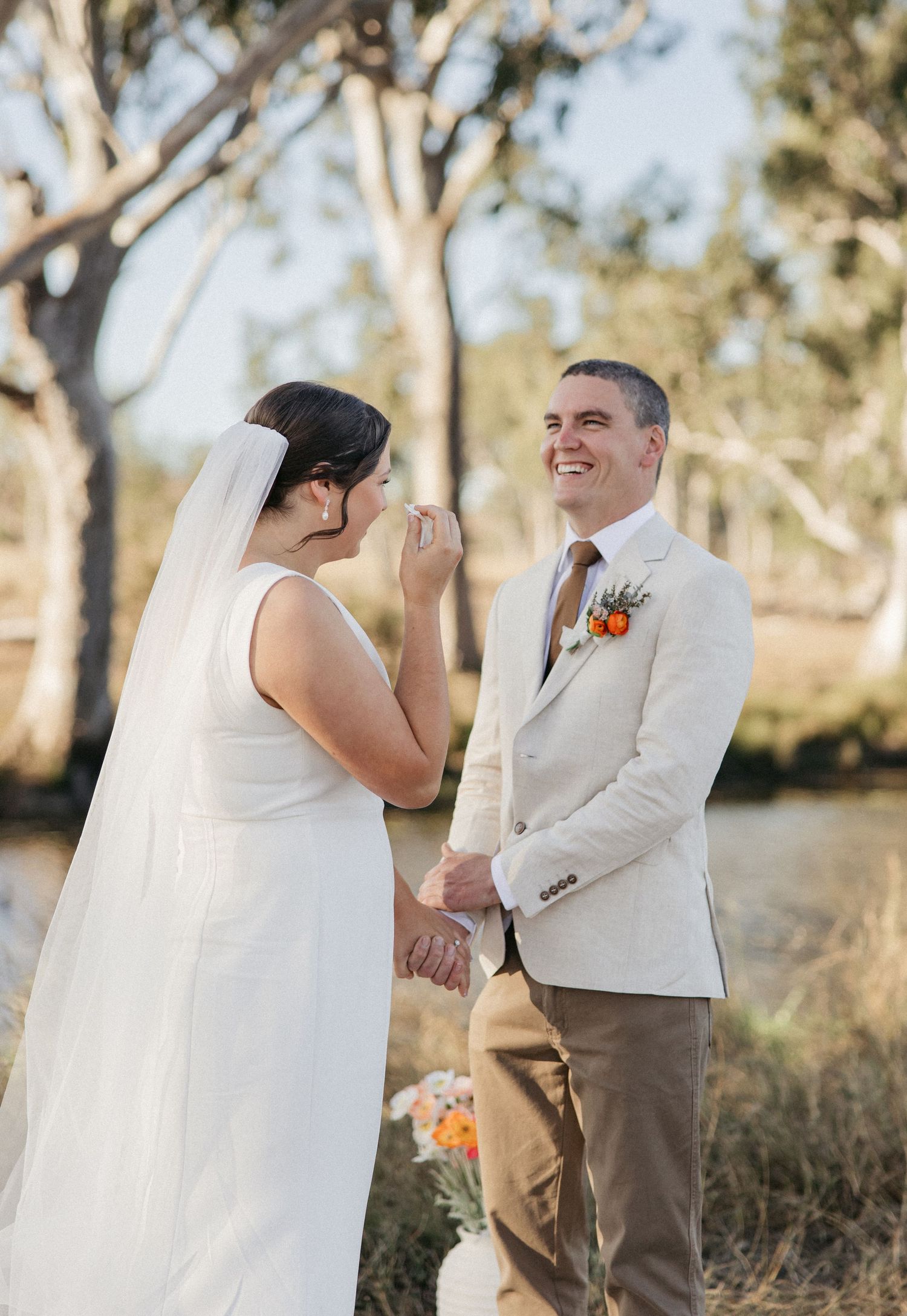 Bride wiping tears while groom smiles during outdoor wedding ceremony surrounded by eucalyptus trees.