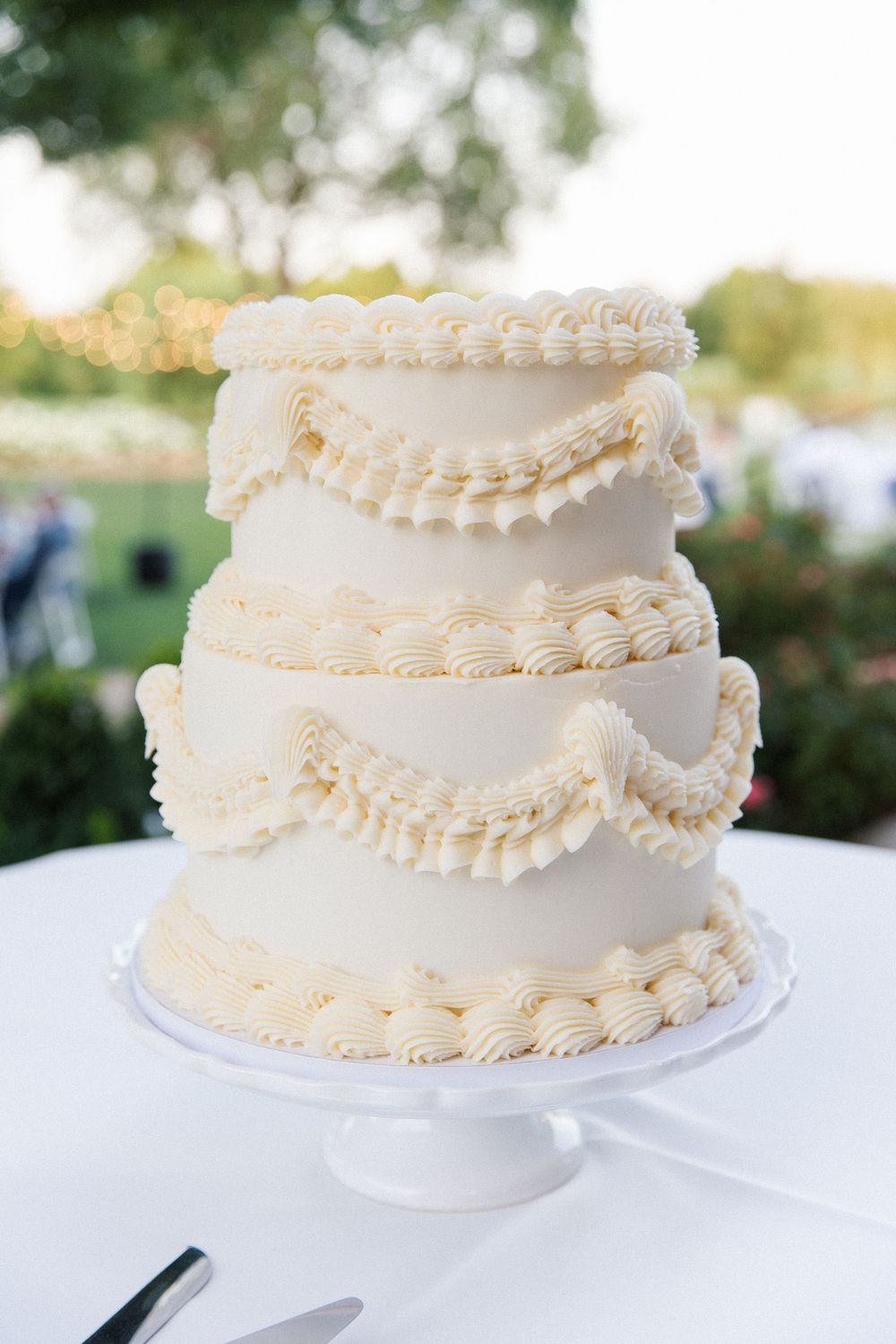 An elegant white wedding cake with delicate piped details and scalloped tiers on a cake stand.
