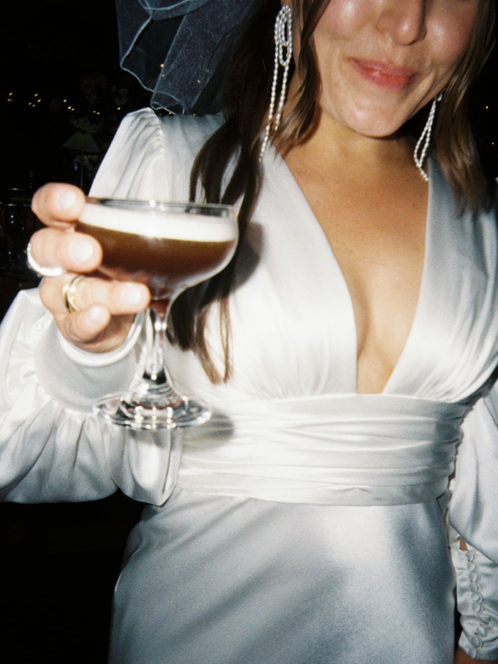 Close-up of champagne glass held by person wearing white dress with crystal earrings.