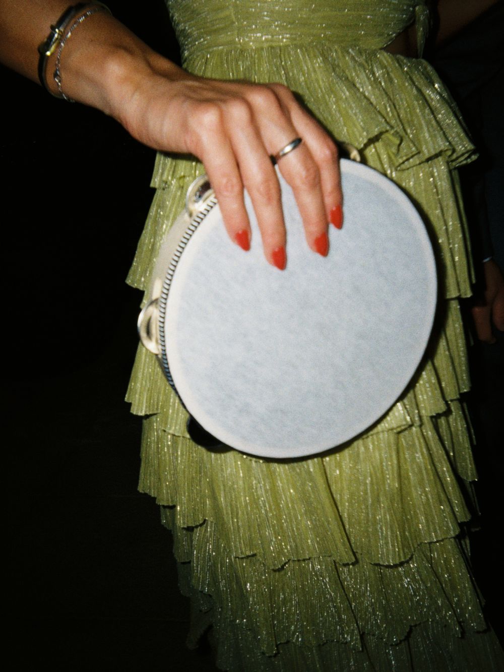 Hand wearing wedding ring holding silver clutch against green sequined dress.