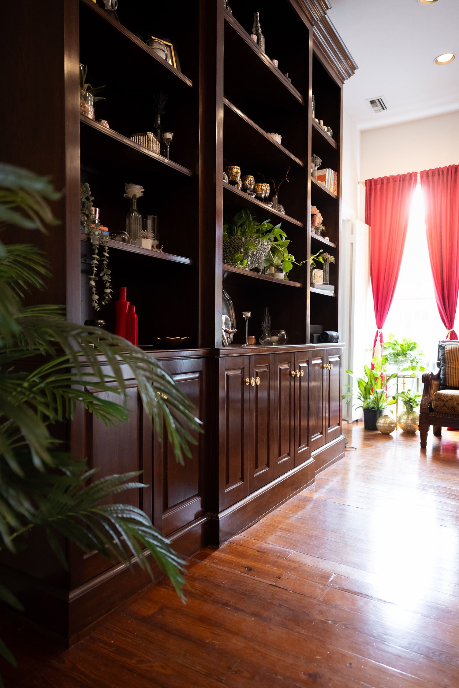 Elegant dark wood built-in shelving lines a hallway with hardwood floors and red curtains at the end.