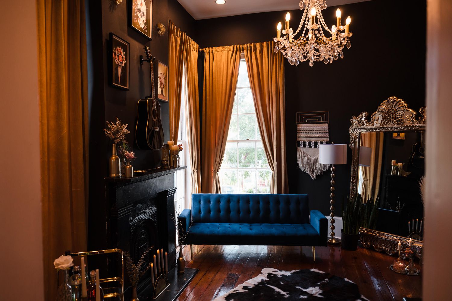 Elegant dark room with teal velvet sofa, gold curtains, ornate mirror and crystal chandelier in vintage style decor.