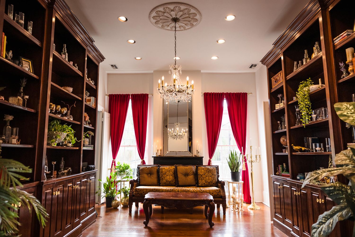 A luxurious wine cellar interior with dark wood shelving, elegant chandeliers, and red curtains creates an upscale atmosphere.
