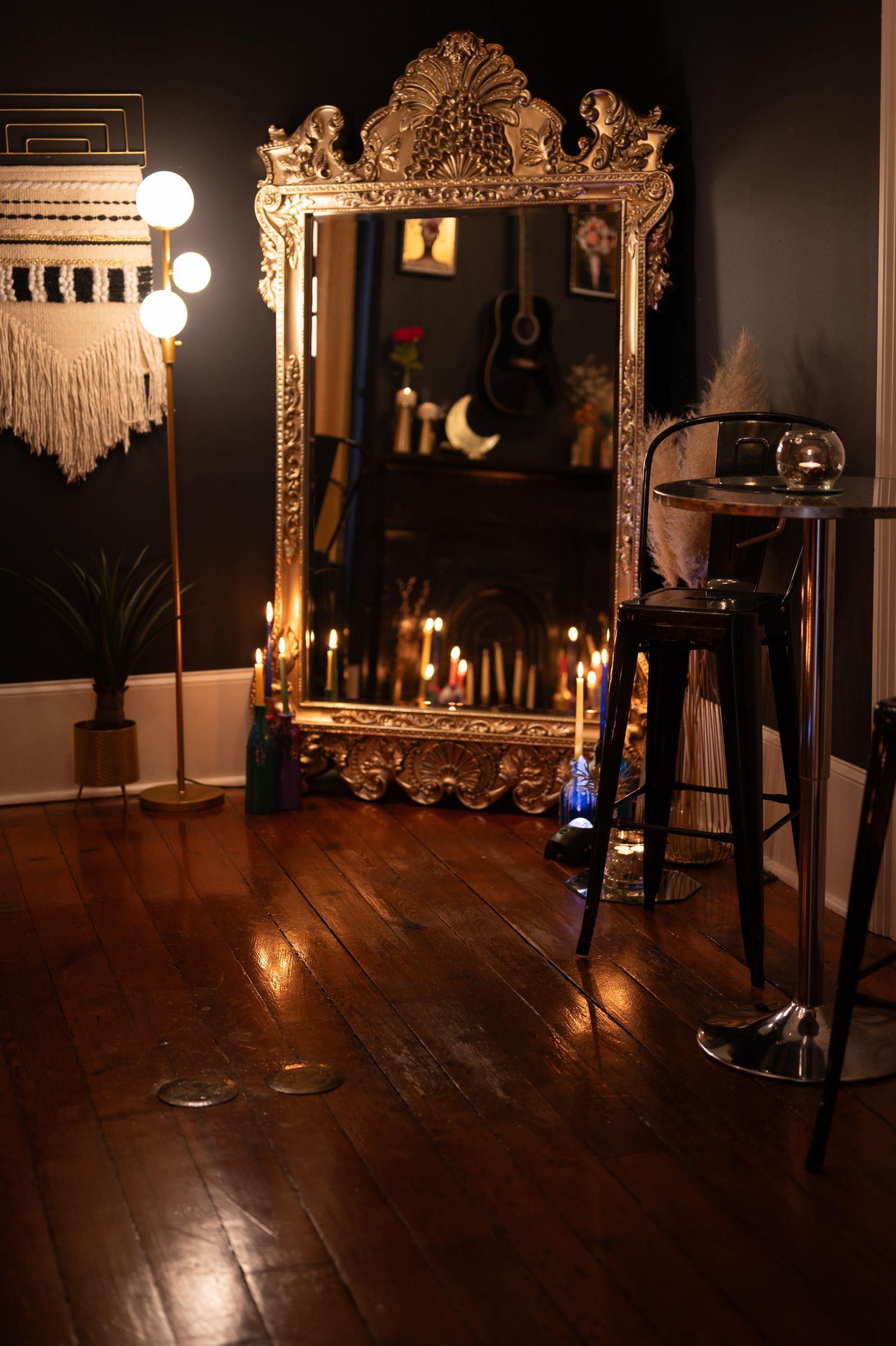 A dark moody photo studio setup with vintage mirrors, macrame decor, and wooden floors illuminated by warm lighting.