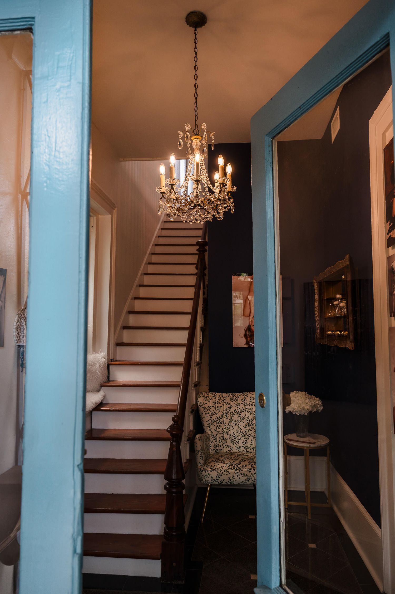 Elegant staircase with white steps and turquoise blue trim leads upward beneath a crystal chandelier in a home interior.