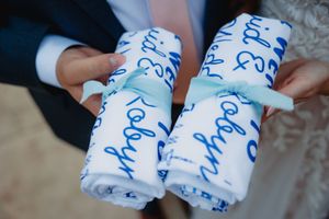 Couple holding personalized white blankets with blue script writing, tied with mint green ribbons, at a wedding.
