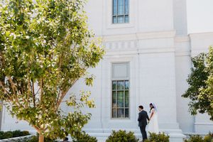 Bride and groom share a romantic moment outside a white classical building surrounded by lush green trees on their wedding day.